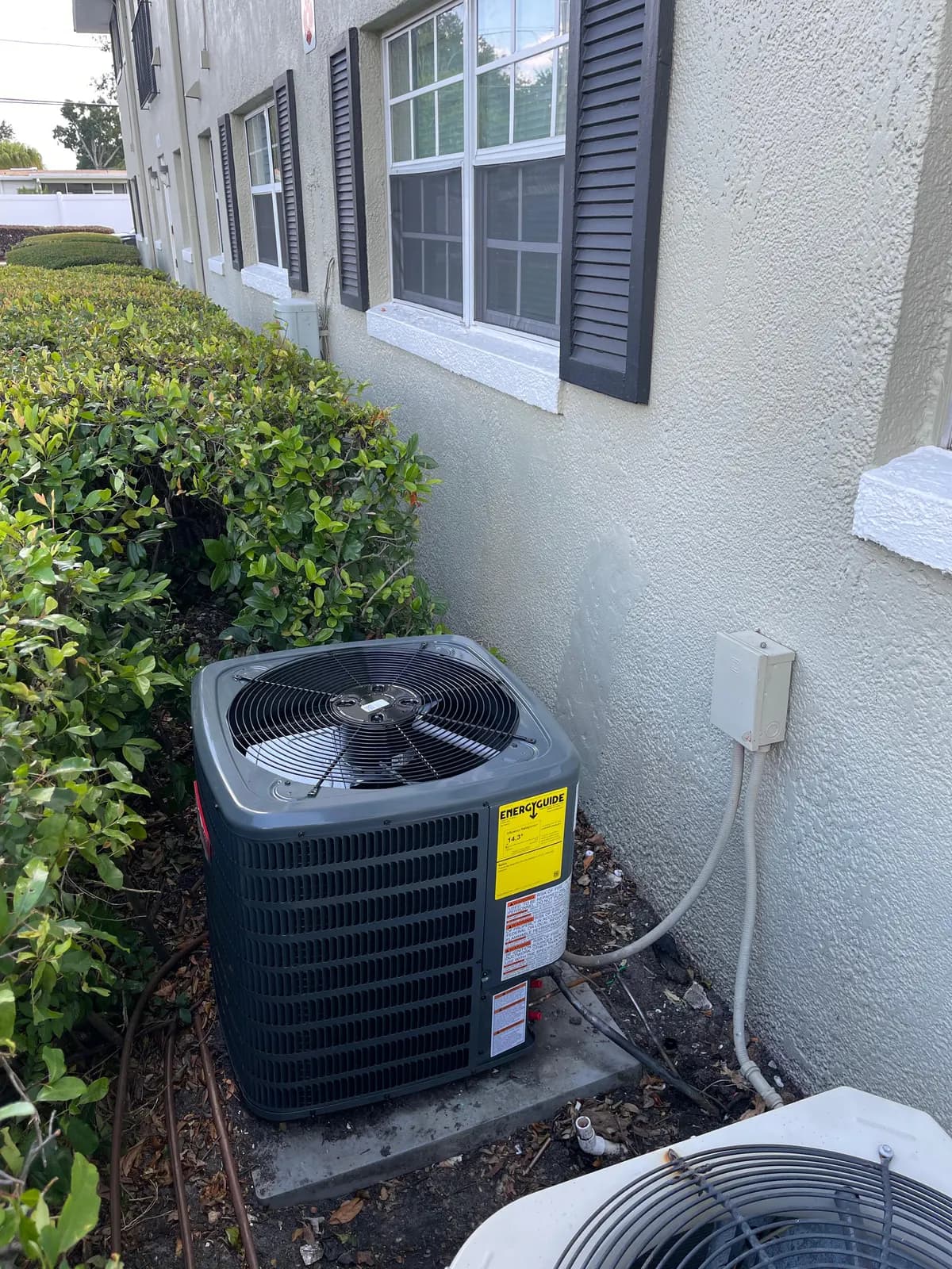 Goodman condenser installed beside a Central Florida home, EnergyGuide label showing a 14.3 SEER2 efficiency rating