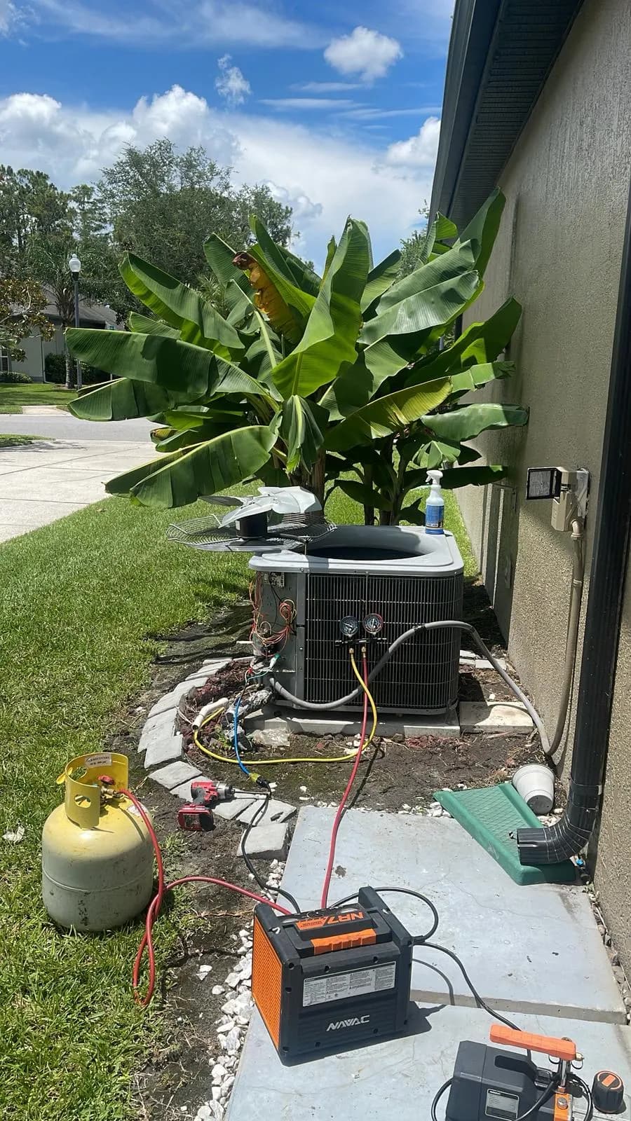 Technician’s manifold gauges, recovery cylinder and vacuum pump connected to a residential condensing unit