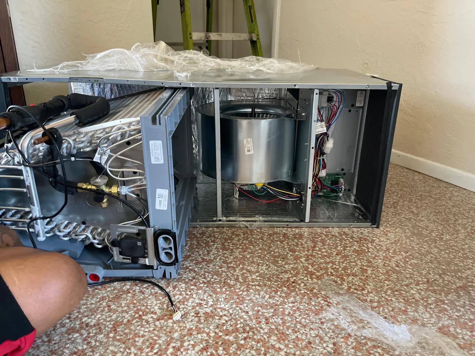 Air handler cabinet opened during installation showing the evaporator coil, blower wheel and control board