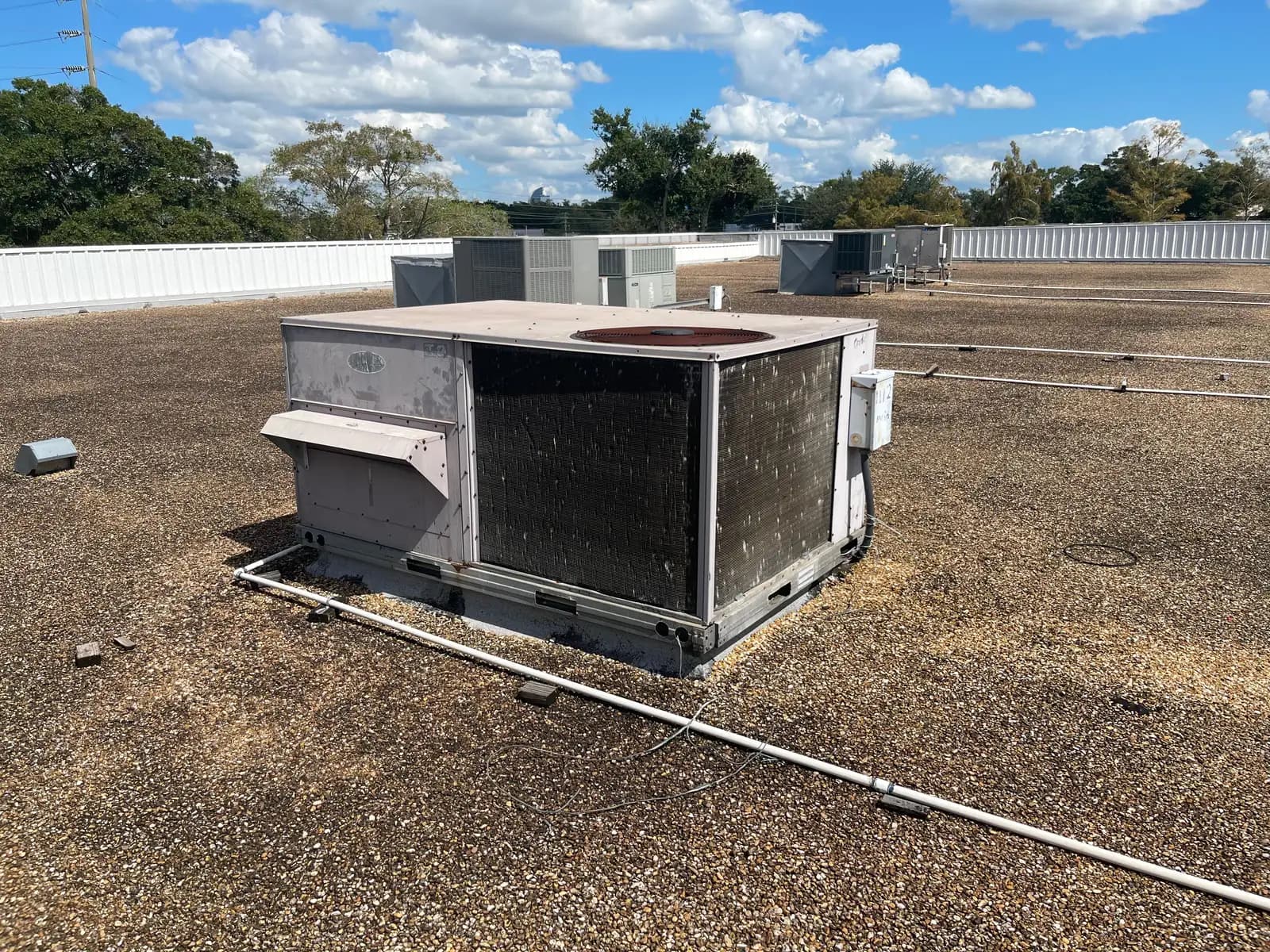 Several commercial rooftop packaged air conditioning units across a flat commercial roof in Central Florida