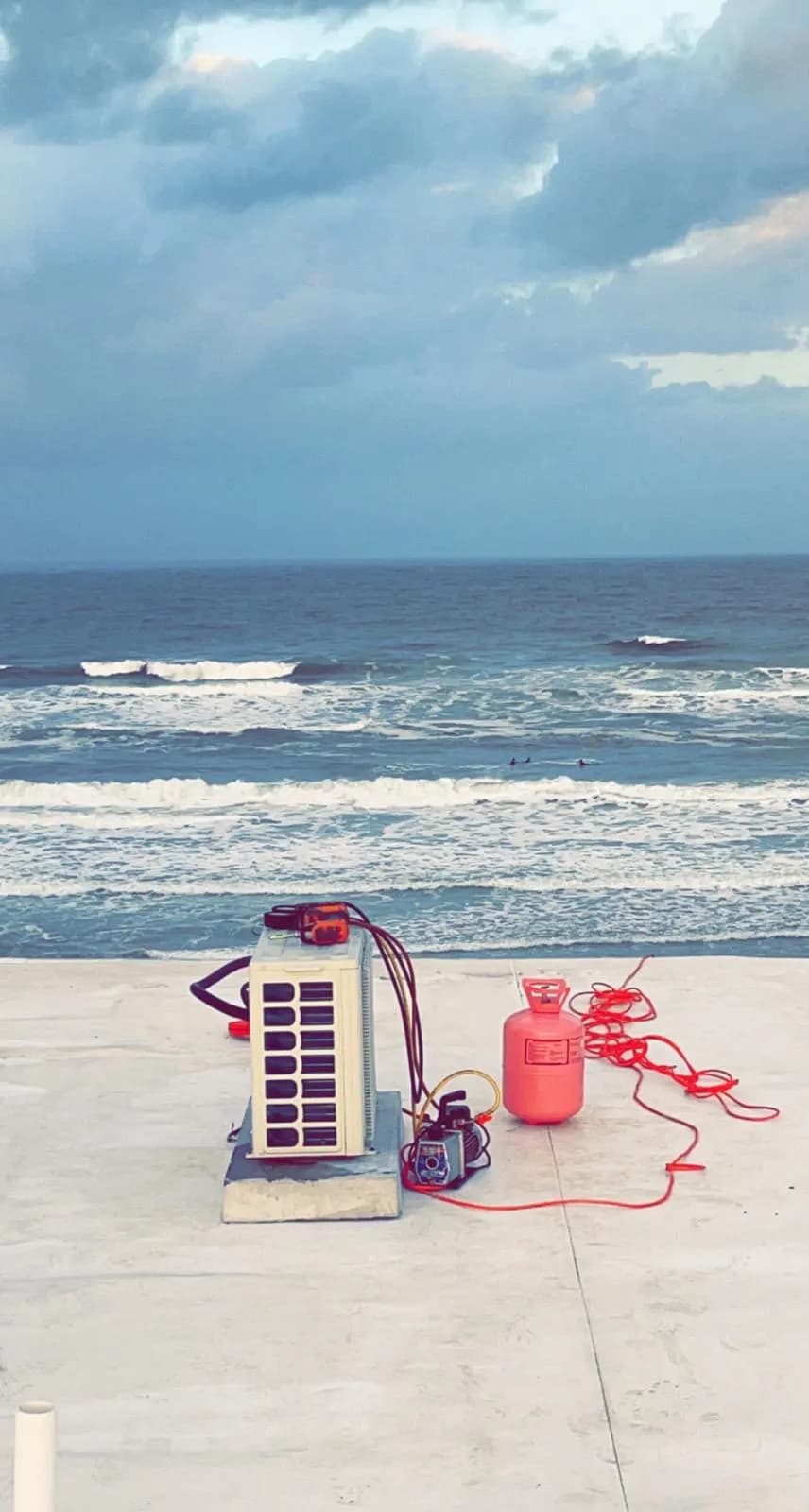 Mini-split condenser being commissioned on an oceanfront concrete deck at dusk